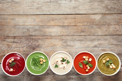 Various cream soups in bowls and space for text on wooden background, top view