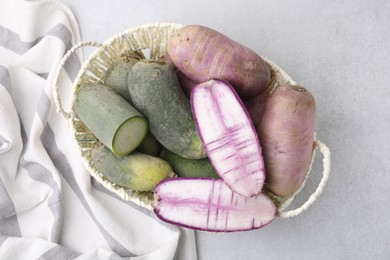 Photo of Purple and green daikon radishes in wicker basket on light grey table, top view