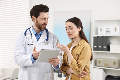 Photo of Doctor with tablet consulting patient during appointment in clinic