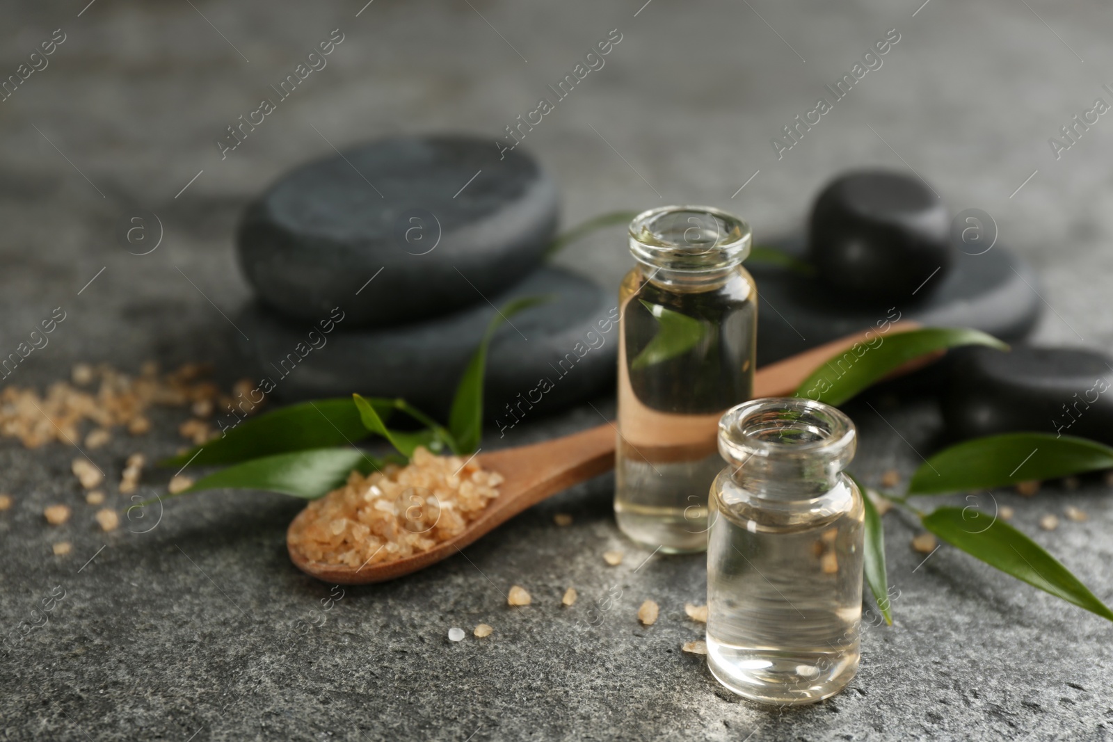 Photo of Beautiful composition with essential oil and spa stones on grey table, closeup