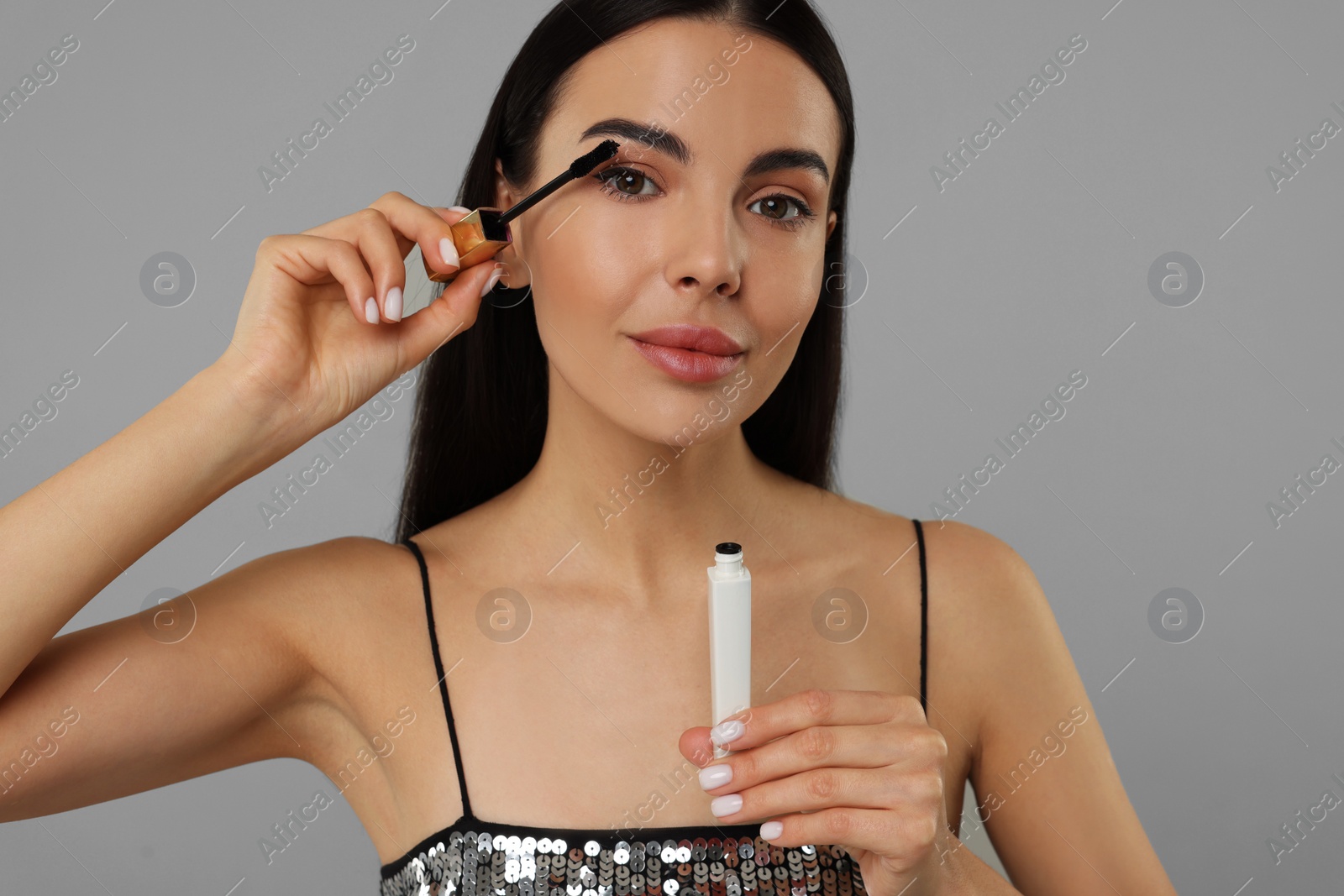 Photo of Beautiful young woman applying mascara on grey background