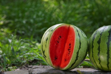 Photo of Delicious whole and cut watermelons on stone surface outdoors. Space for text