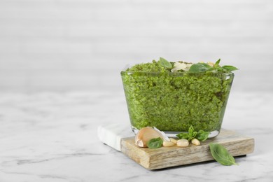 Photo of Delicious pesto sauce in bowl on white marble table, closeup. Space for text