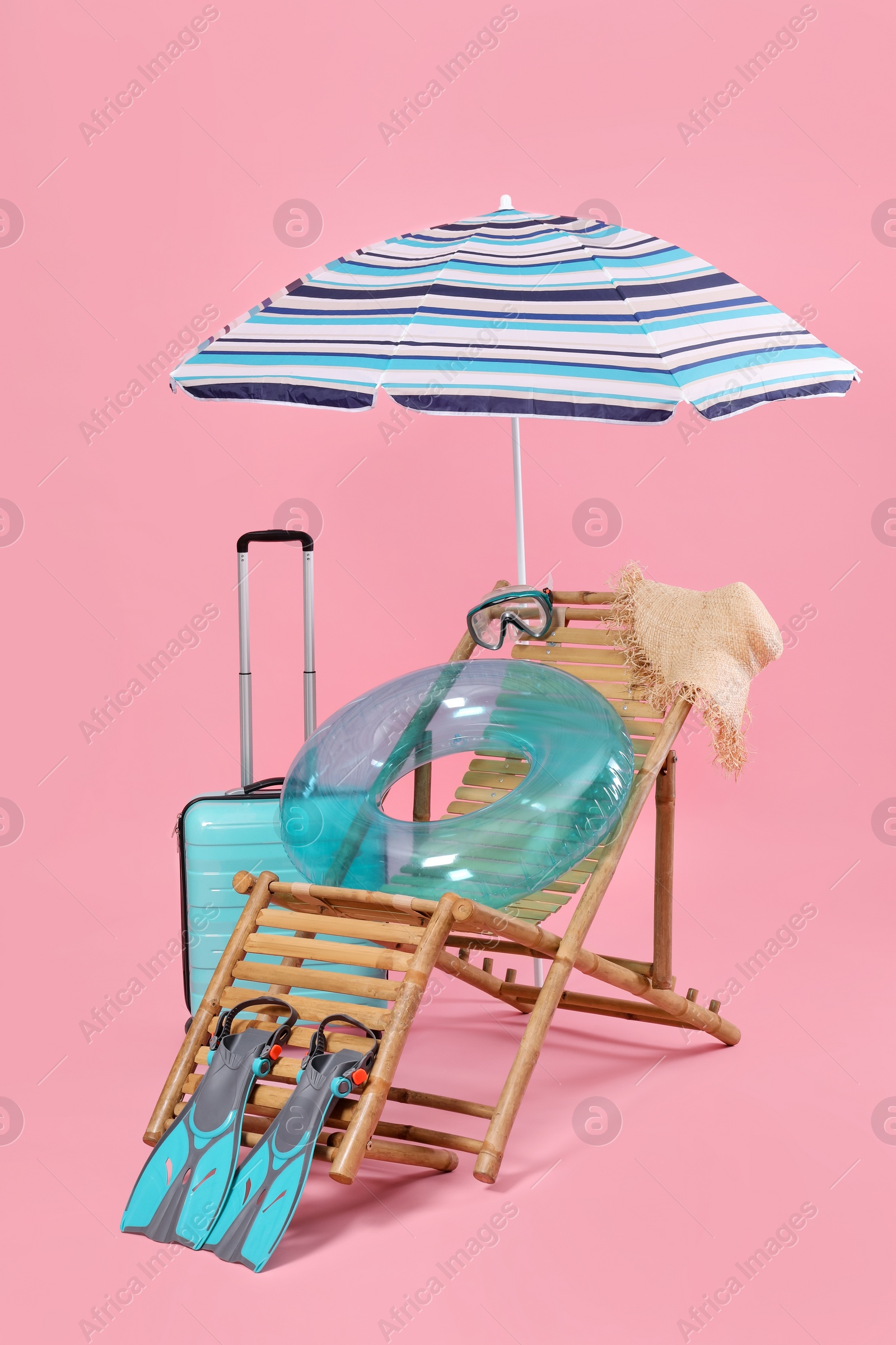 Photo of Deck chair, suitcase and beach accessories on pink background