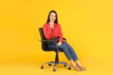 Young woman sitting in comfortable office chair on yellow background