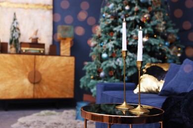 Pair of beautiful candlesticks on glass table and Christmas decor in room, space for text