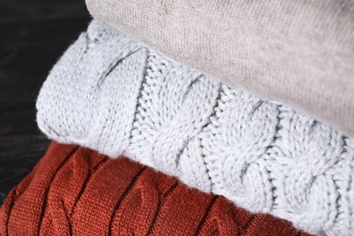 Image of Stack of folded warm sweaters on black wooden table, closeup