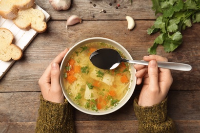 Woman eating fresh homemade chicken soup at table, top view