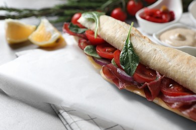 Delicious sandwich with bresaola, tomato, onion and cheese on light grey table, closeup. Space for text