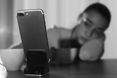 Lonely woman looking at smartphone on foreground, space for text. Black and white effect