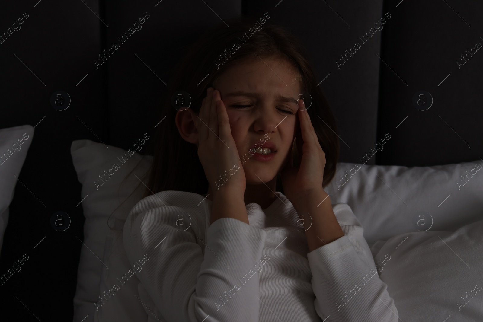 Photo of Little girl suffering from headache in bed at night