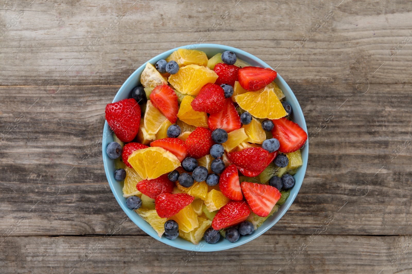 Photo of Delicious fresh fruit salad in bowl on wooden table, top view