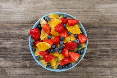 Delicious fresh fruit salad in bowl on wooden table, top view