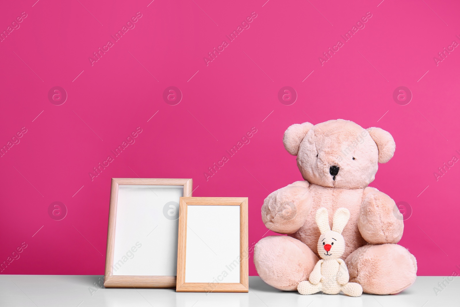 Photo of Photo frames and adorable toys on table against color background, space for text. Child room elements