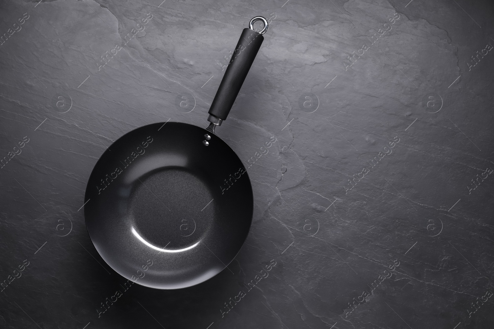 Photo of Empty iron wok on black textured table, top view. Space for text