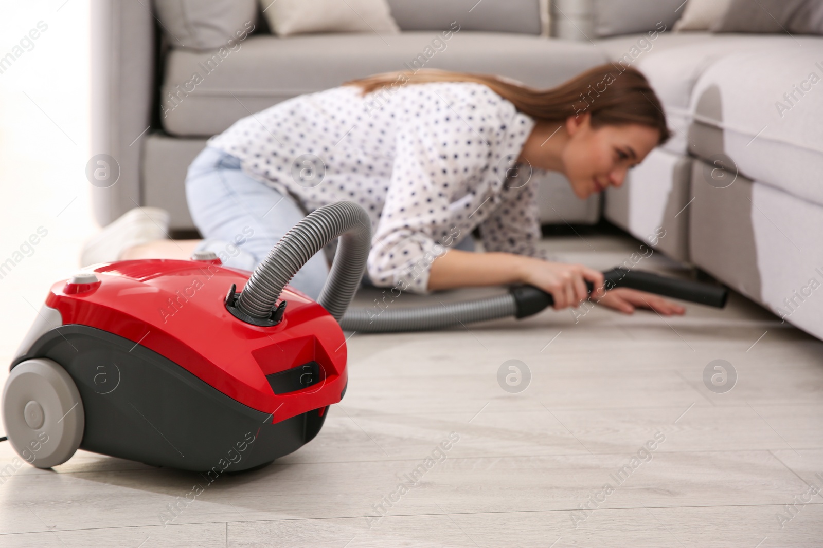Photo of Young woman using vacuum cleaner at home