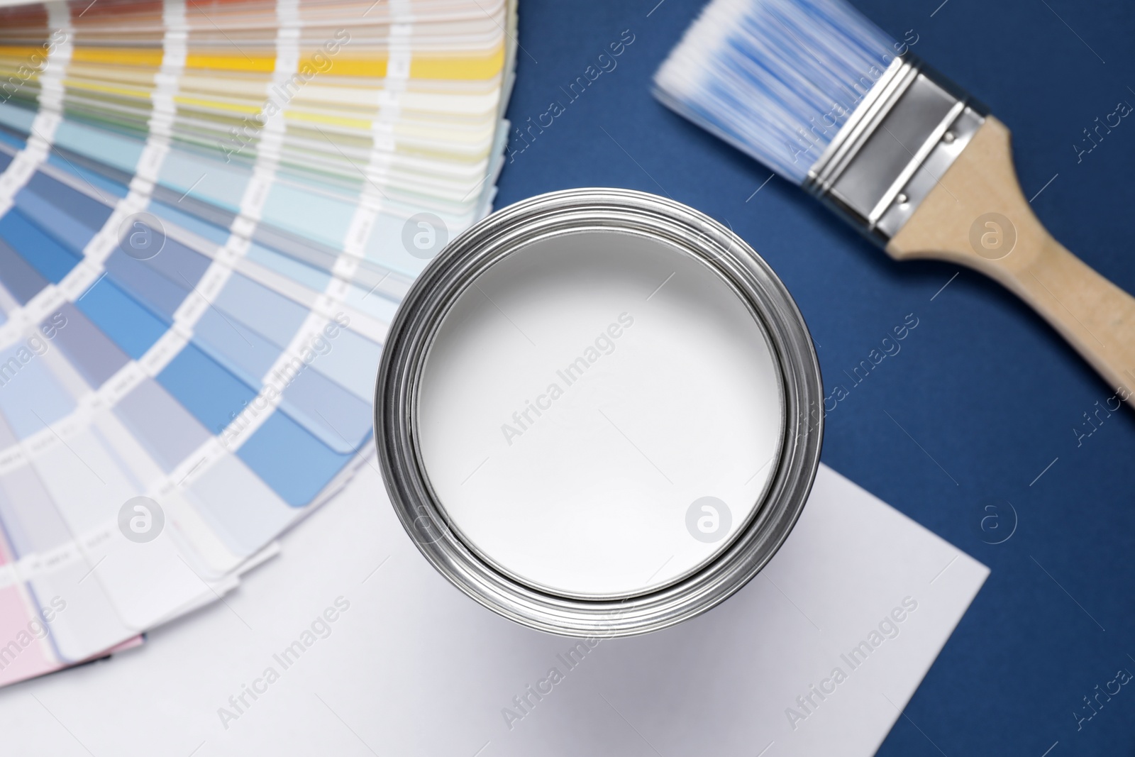 Photo of Can with white paint, brush and color palette on blue background, flat lay