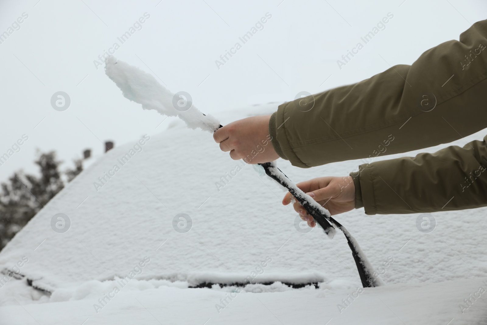 Photo of Woman cleaning car wiper blade covered with snow outdoors, closeup