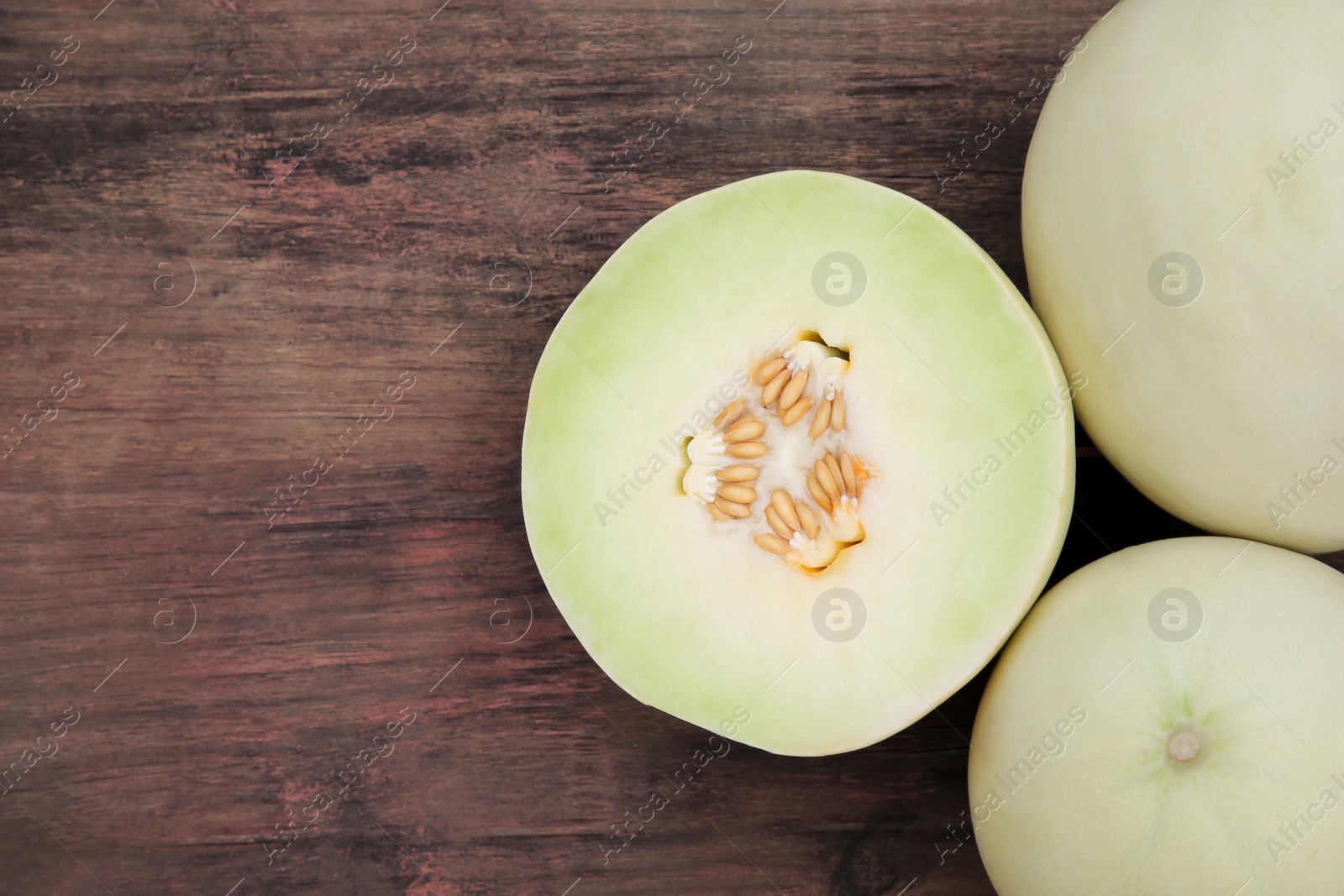 Photo of Whole and cut fresh ripe melons on wooden table, flat lay. Space for text