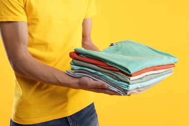 Photo of Dry-cleaning delivery. Courier holding folded clothes on orange background, closeup
