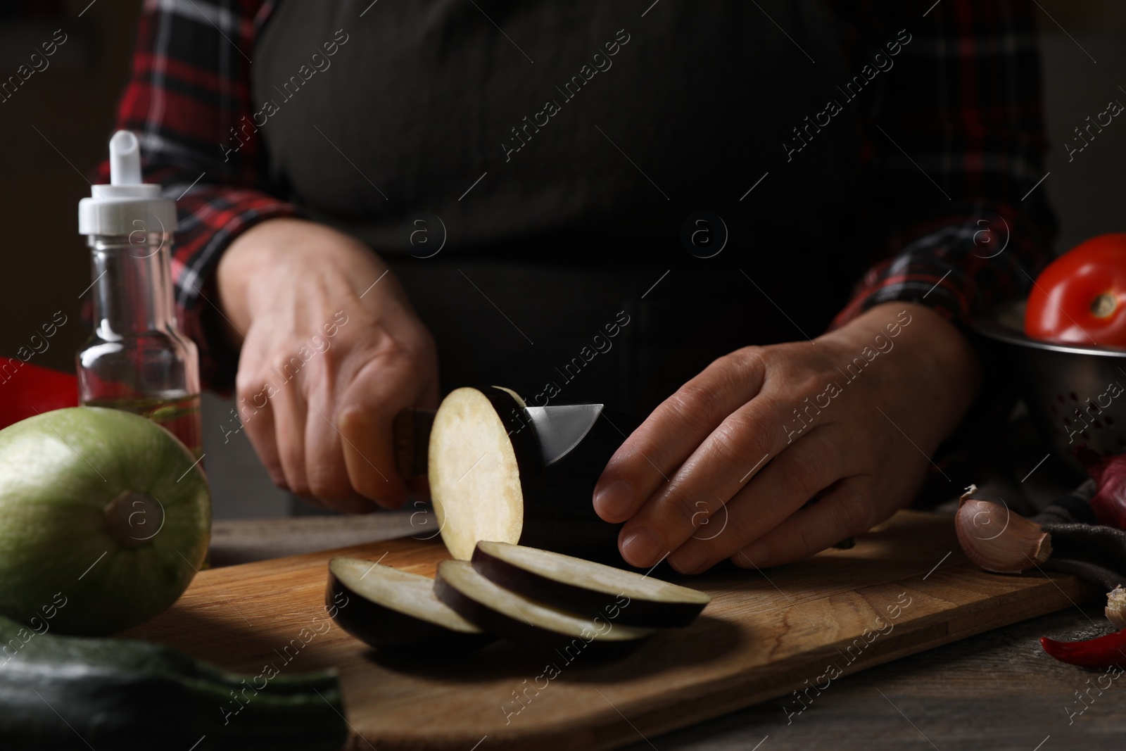 Photo of Cooking delicious ratatouille. Woman cutting fresh eggplant at wooden table, closeup