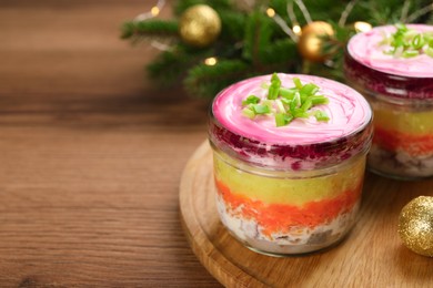 Photo of Glass jars with herring under fur coat and Christmas decor on wooden table, space for text. Traditional Russian salad