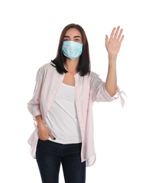 Photo of Young woman in protective mask showing hello gesture on white background. Keeping social distance during coronavirus pandemic