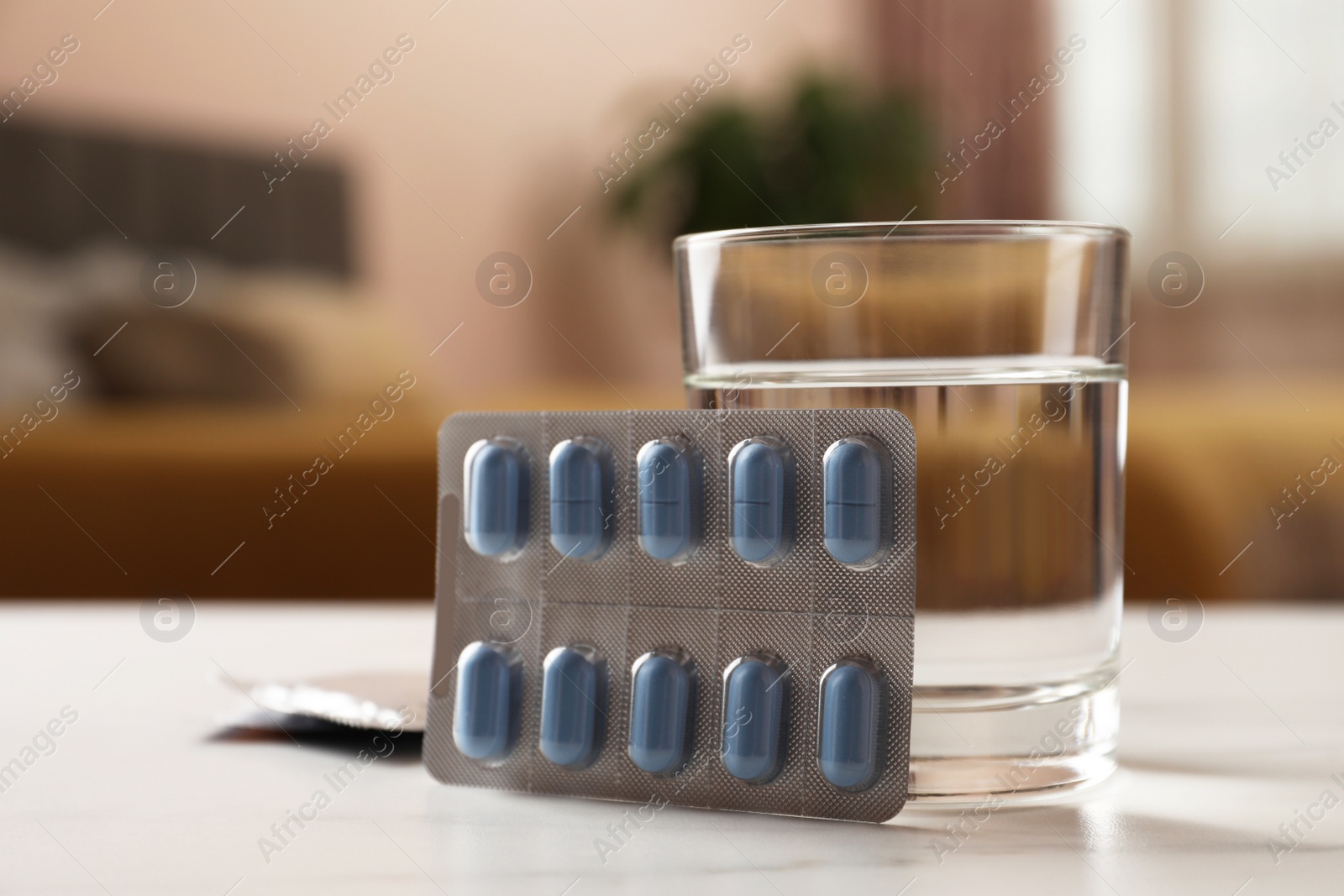 Photo of Glass of water, condoms and pills on white table indoors, closeup. Potency problem concept