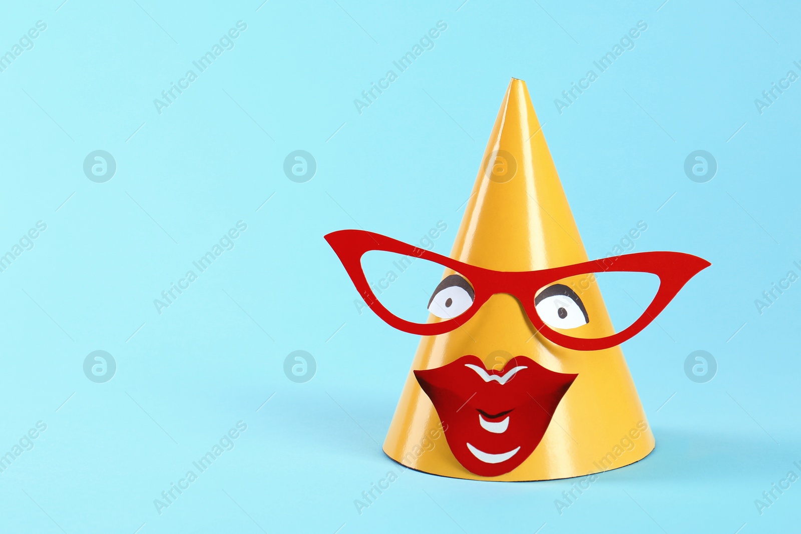 Photo of Handmade party hat with funny face on light blue background. Space for text