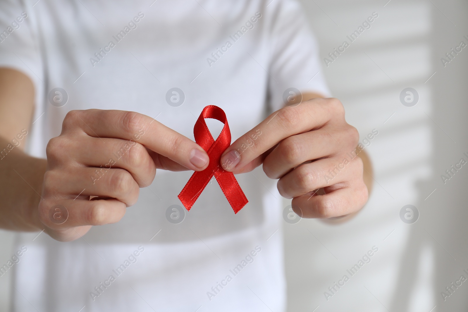 Photo of Woman holding red awareness ribbon on light background, closeup. World AIDS disease day