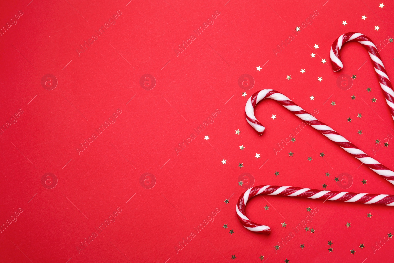 Photo of Delicious Christmas candy canes and confetti on red background, flat lay. Space for text