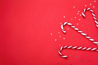 Delicious Christmas candy canes and confetti on red background, flat lay. Space for text