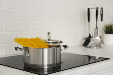 Photo of Saucepan with uncooked pasta on stove in kitchen