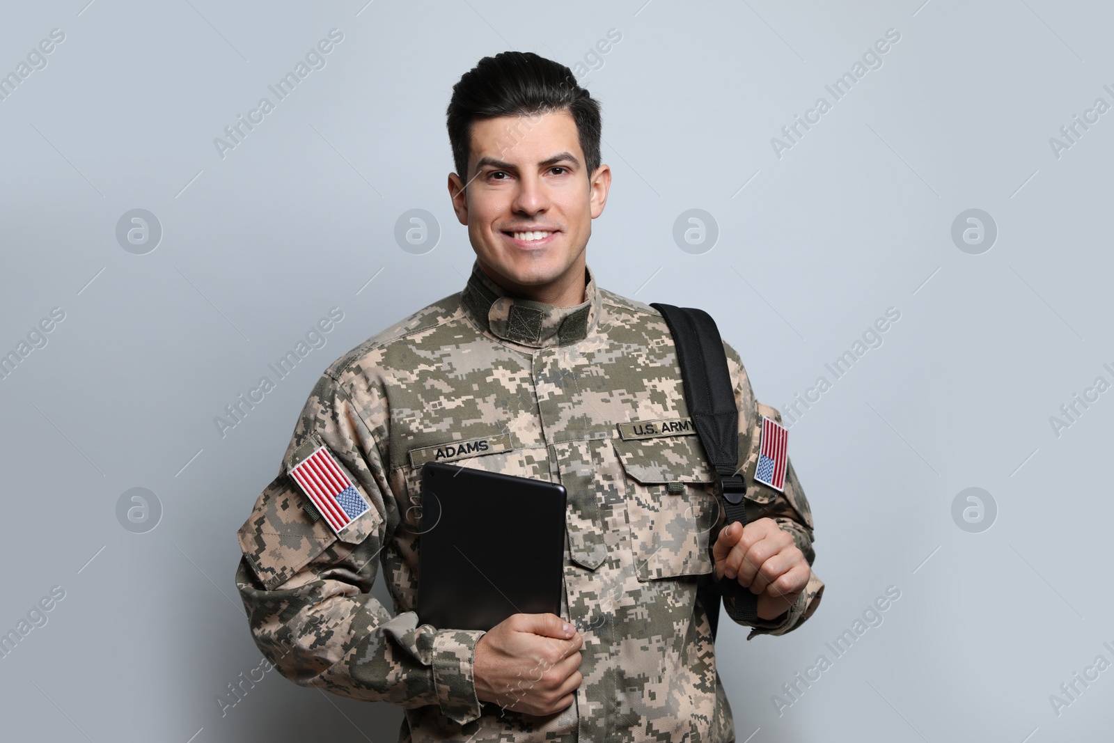 Photo of Cadet with backpack and tablet on light grey background. Military education