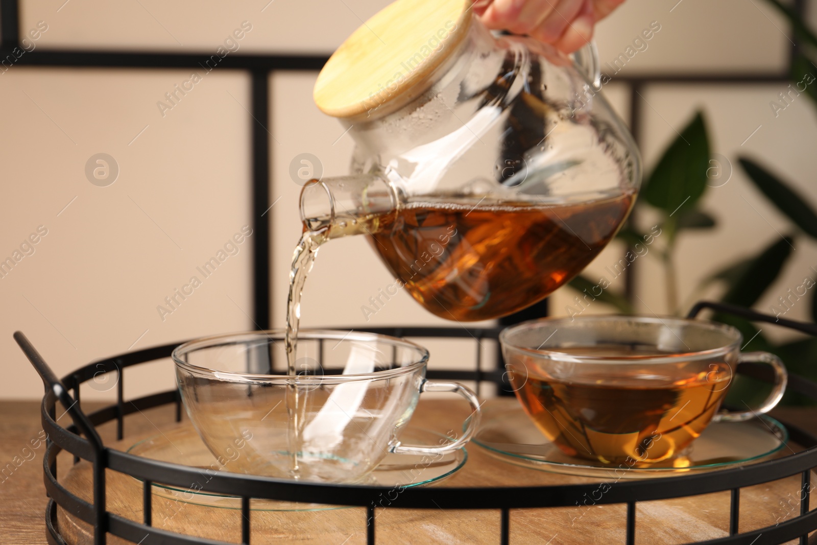 Photo of Woman pouring tasty tea into glass cup at table, closeup