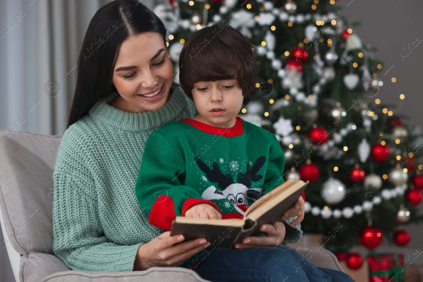 Photo of Mother with her cute son reading book in room decorated for Christmas