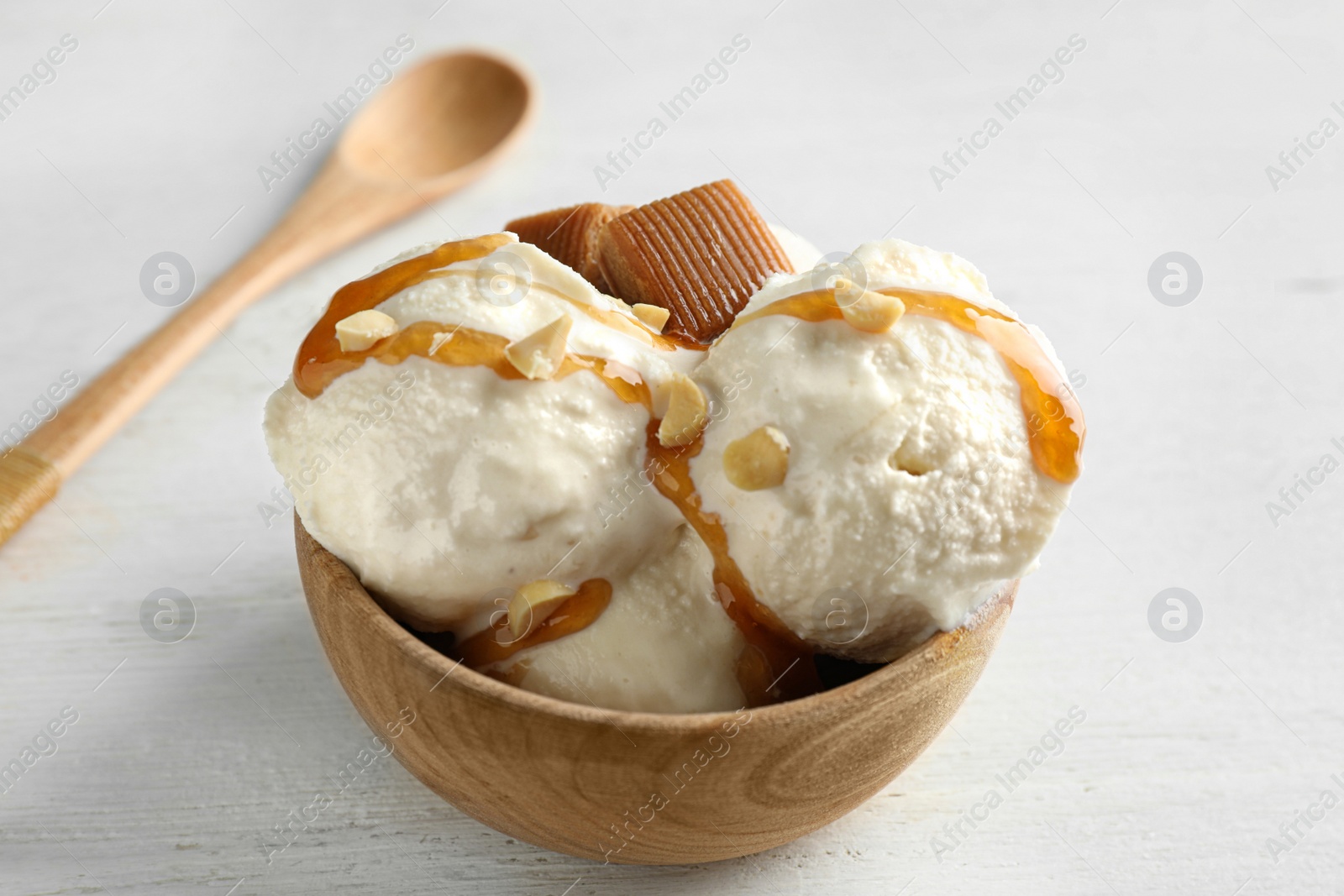 Photo of Delicious ice cream with caramel candies in bowl on white wooden table