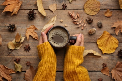 Photo of Woman with cup of hot drink at wooden table, top view. Cozy autumn atmosphere