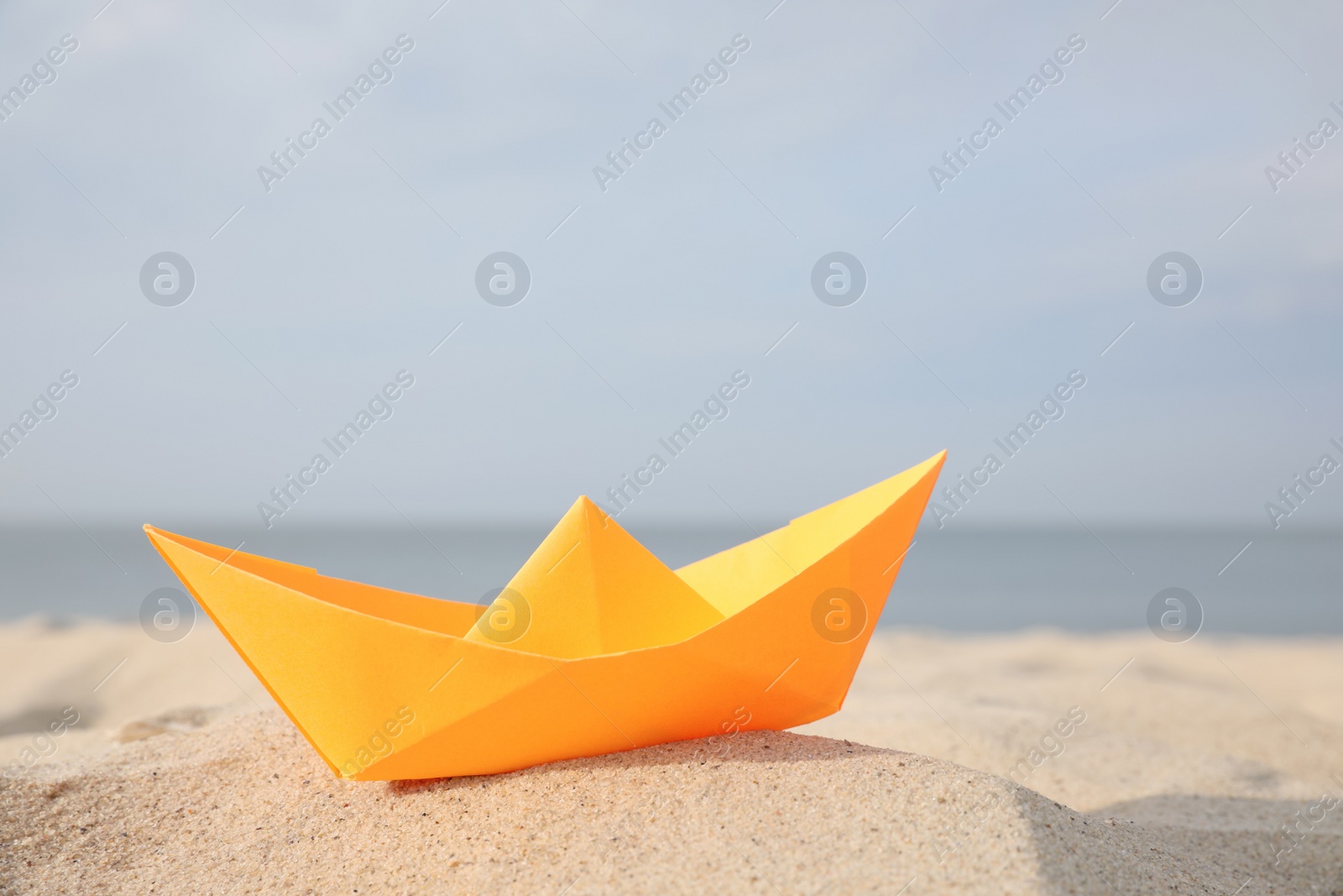 Photo of Orange paper boat on sandy beach near sea, space for text