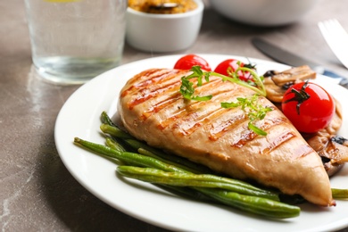 Photo of Tasty grilled chicken fillet with green beans, tomatoes and arugula on table, closeup