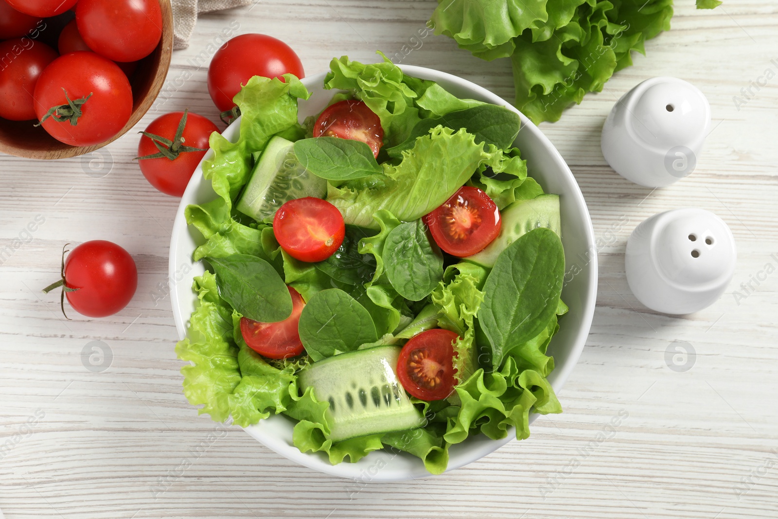 Photo of Delicious vegetable salad, cherry tomatoes, lettuce, pepper and shakers on white wooden table, flat lay