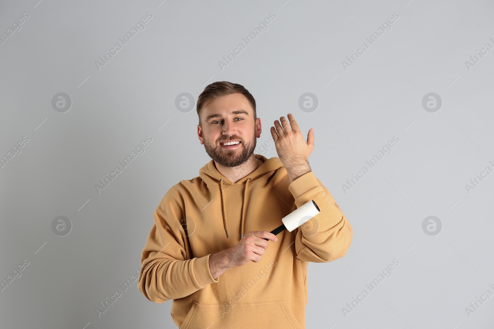 Photo of Young man cleaning clothes with lint roller on grey background