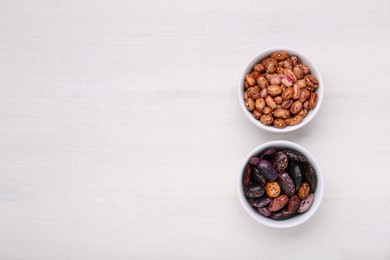 Photo of Bowls with different types of beans on white wooden table, flat lay. Space for text