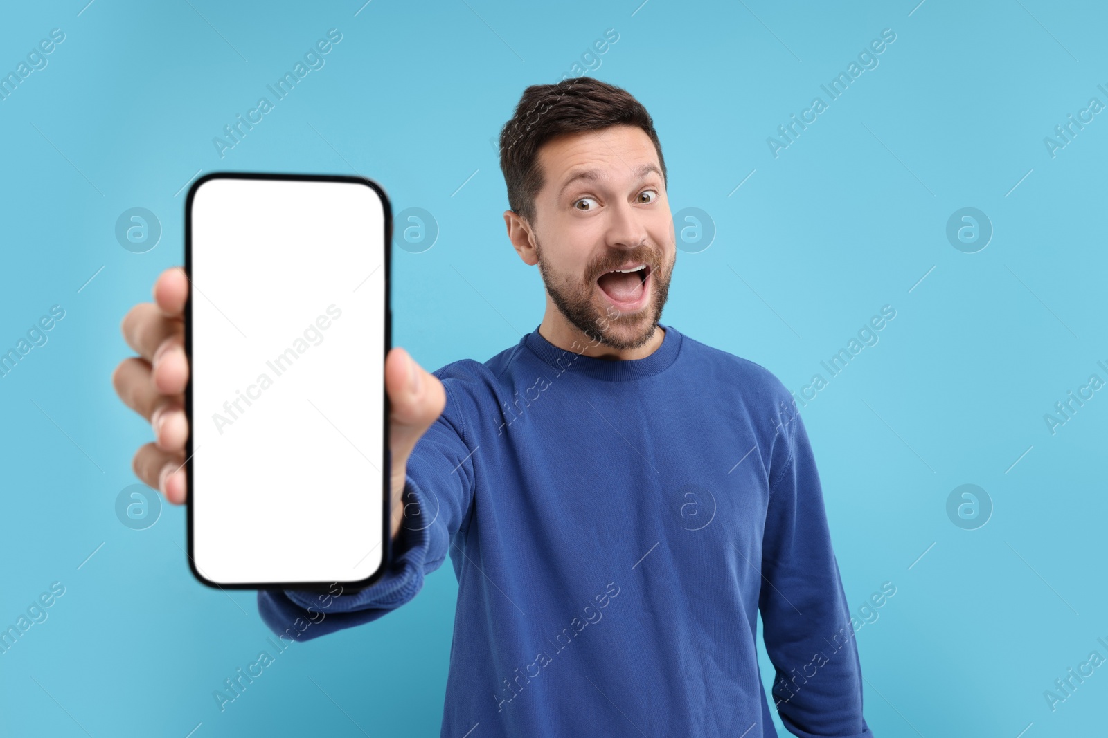 Photo of Surprised man showing smartphone in hand on light blue background