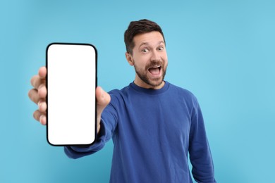 Surprised man showing smartphone in hand on light blue background