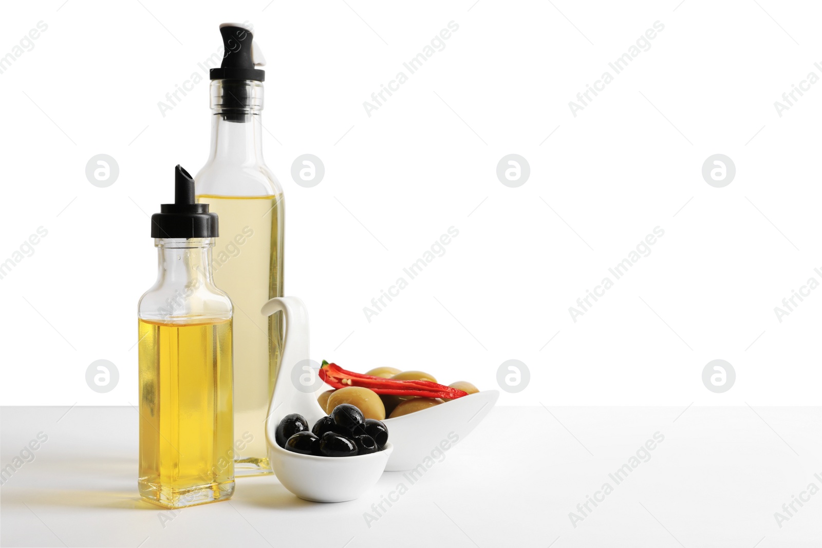 Photo of Bottles of different cooking oils and olives on white background