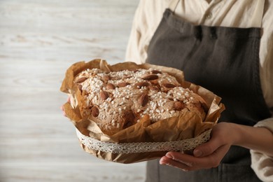 Photo of Woman with delicious Italian Easter dove cake (traditional Colomba di Pasqua) near white wooden wall, closeup