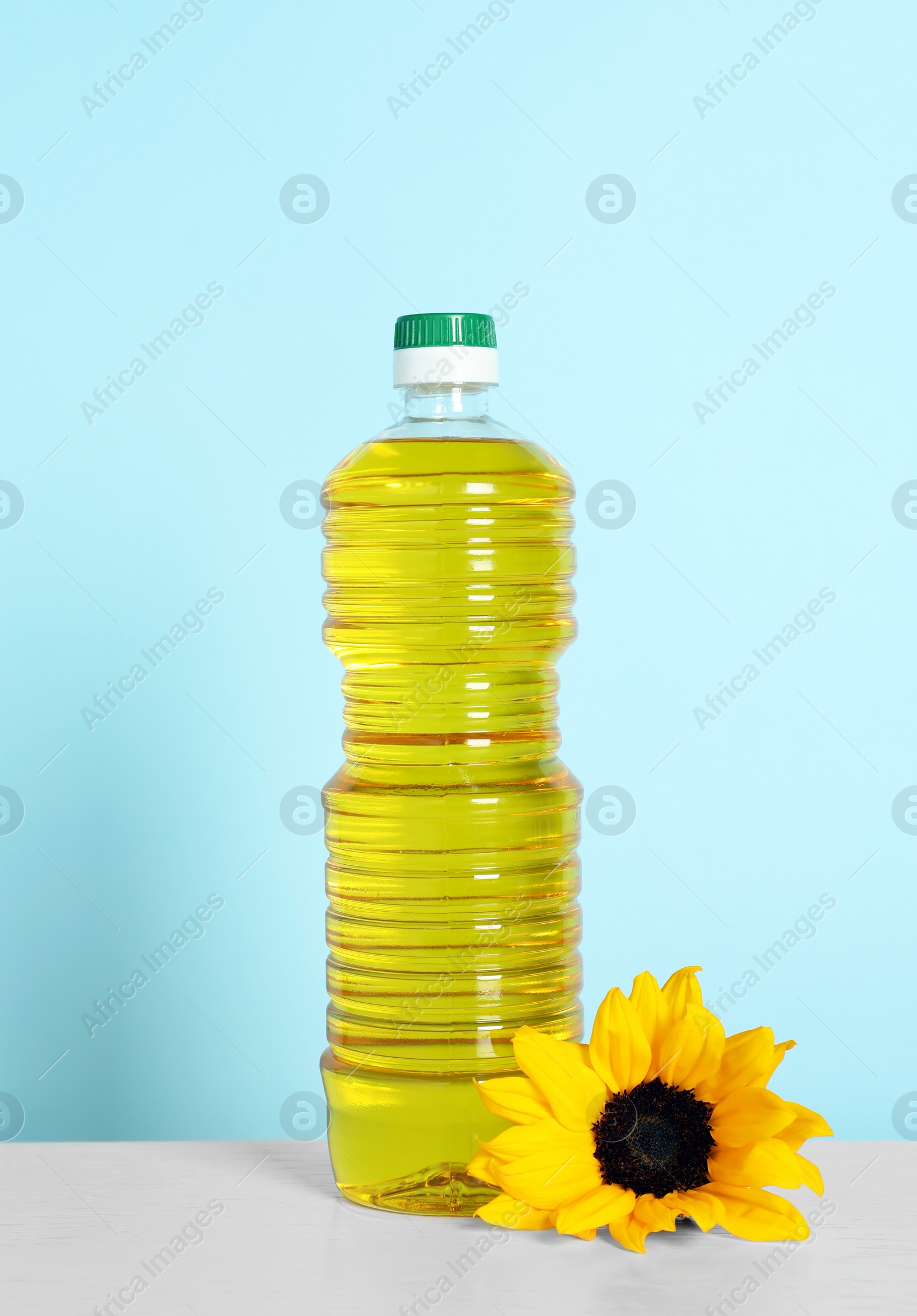 Photo of Bottle of cooking oil and sunflower on white table