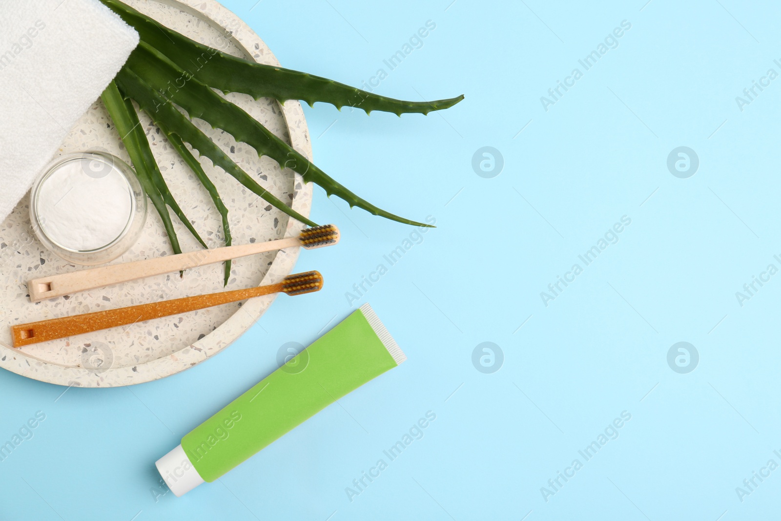 Photo of Tube of toothpaste, fresh aloe and care products on light blue background, flat lay. Space for text