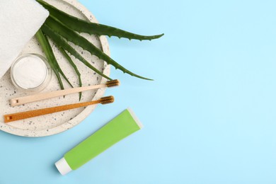 Photo of Tube of toothpaste, fresh aloe and care products on light blue background, flat lay. Space for text